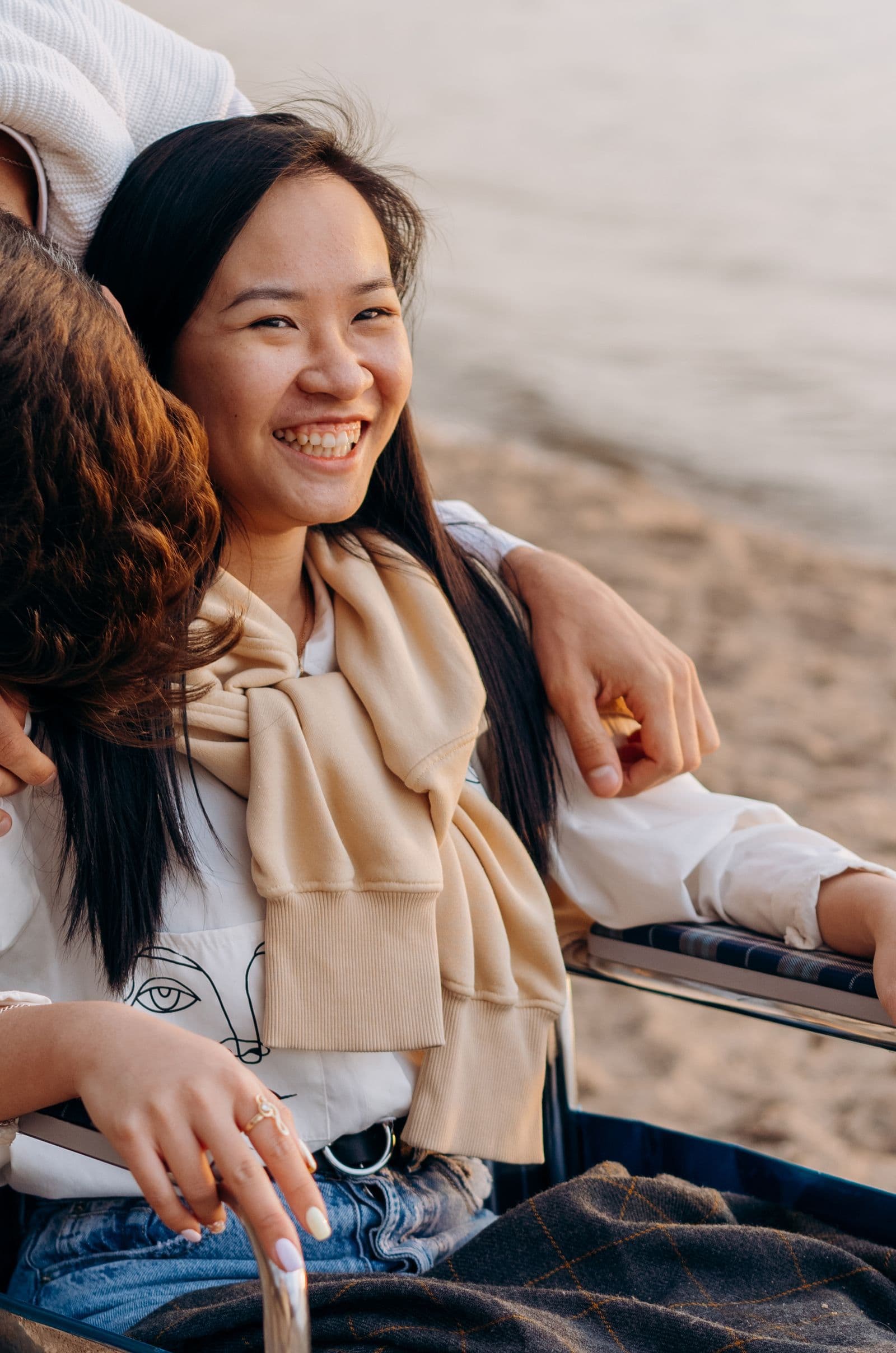 A joyful adult wheelchair user relaxing on a beach at sunset with friends