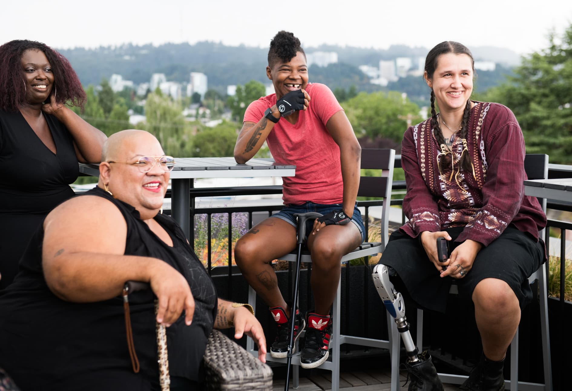 Four adults, most of them people of colour and several visibly disabled, laughing together on a rooftop deck